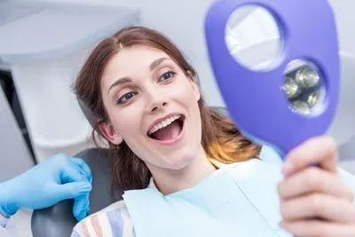 Evergreen Smile Studio patient smiling in the mirror after her dental appointment